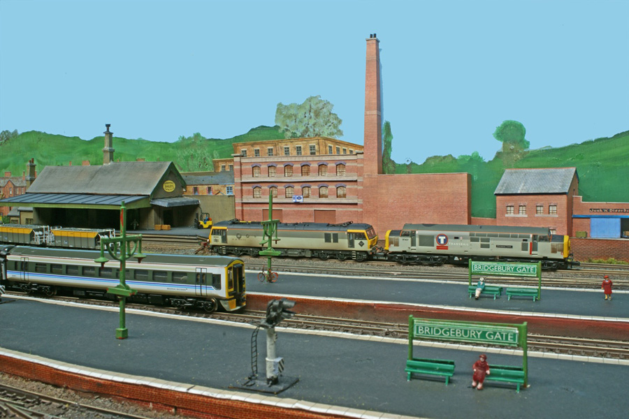 A Regional Railways DMU arrives at Bridgebury Gate's main platform while two sector-liveried locos are stables at the back of the loop lines.