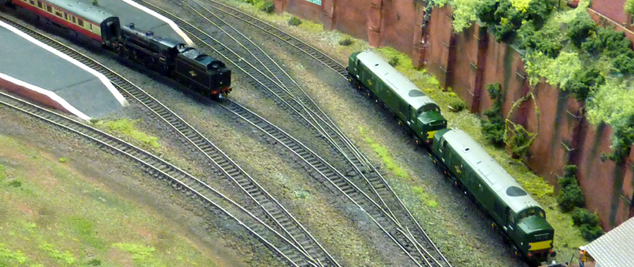 A pair of ex-works Class 37s wait at the stabling point for their next duty (with their drivers in the signal box, making tea again), while a steam-hauled rail tour pauses at Bridgebury Station for a photo opportunity.